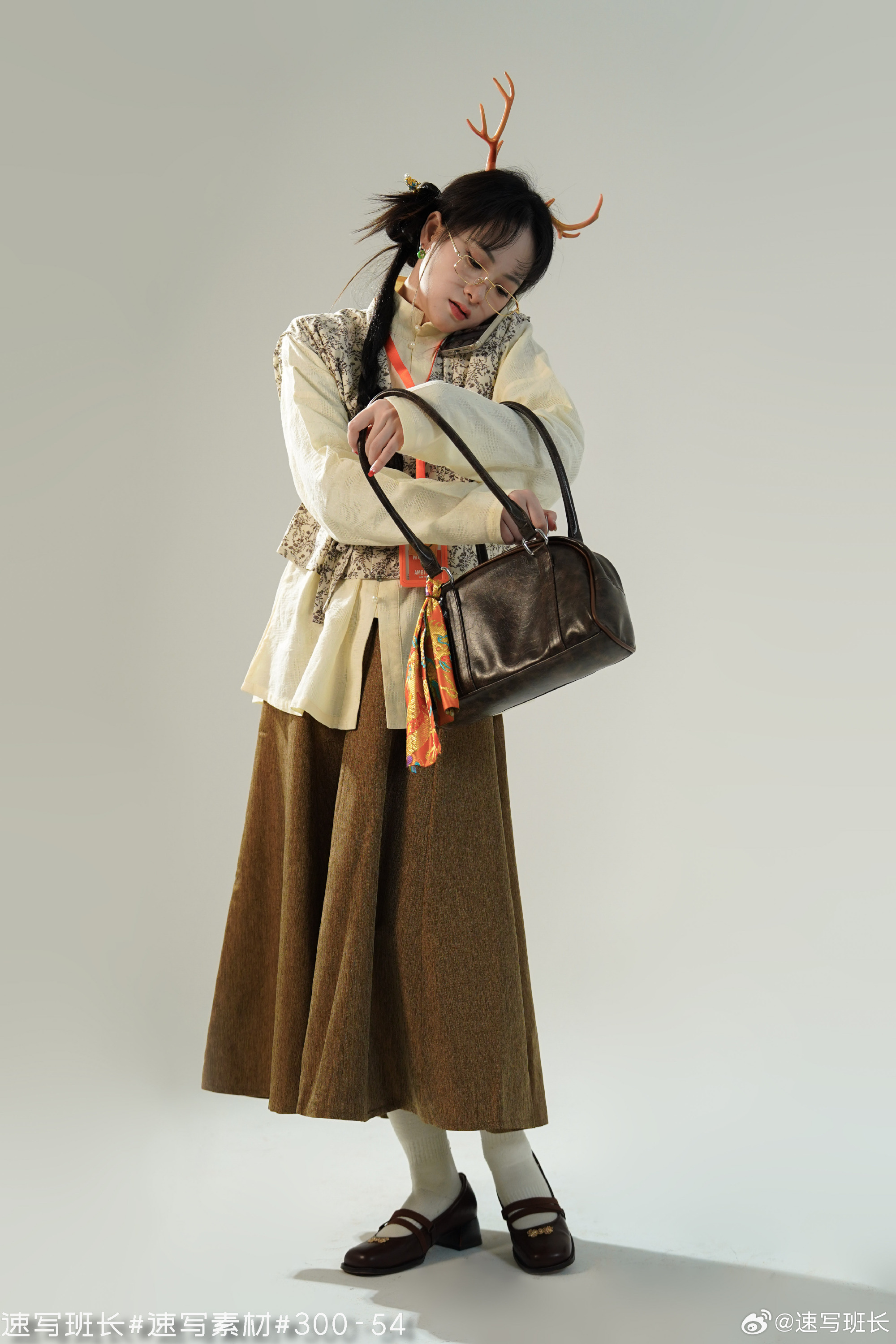 a woman in a studio setting, wearing a white blouse, brown vest and long skirt, paired with black shoes and white socks, and holding a dark brown leather bag. she is posing with her head down, adorned with decorative antlers. the lighting is soft, creating a gentle and diffused illumination. the overall style suggests a quirky and whimsical aesthetic.