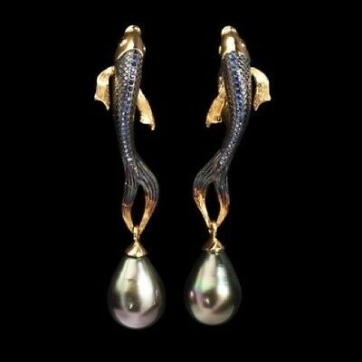 two earrings of fish with pearl drops are positioned close together in the center of the frame against a black background. the earrings are designed as golden fish, each dangling a single pearl. the fish has fins that are also golden, and the pearls are teardropshaped and have a silverygrey hue.