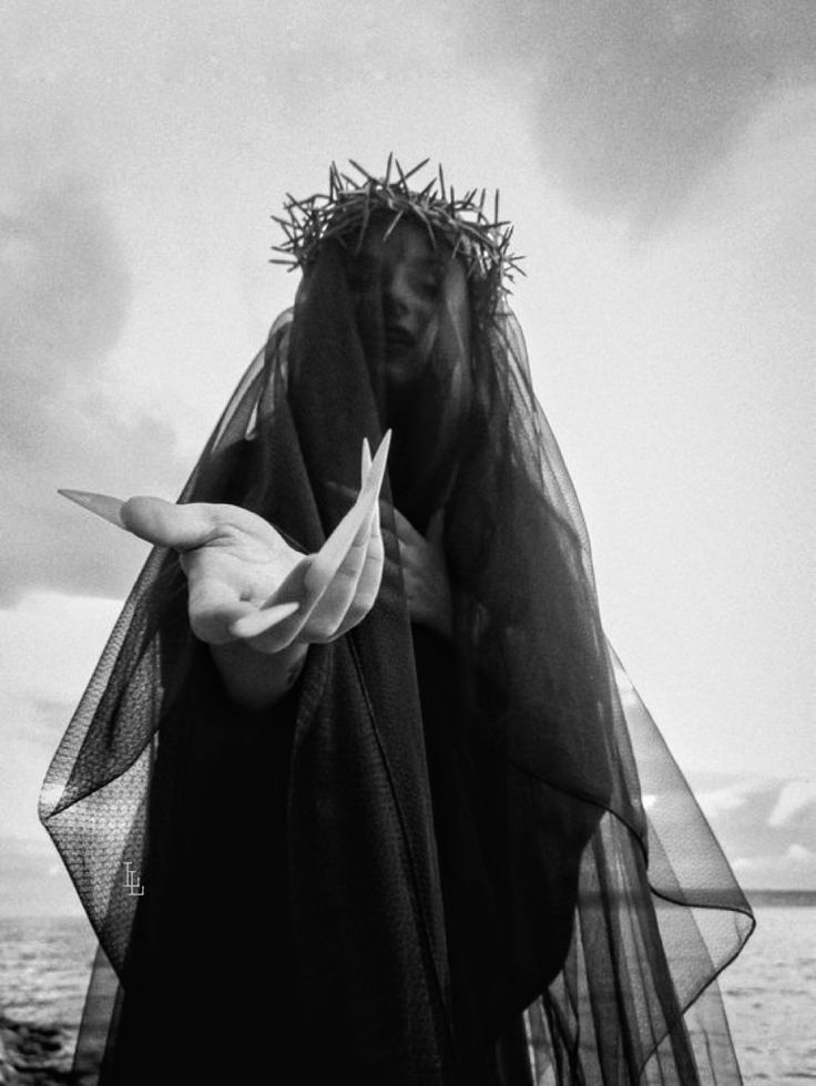 a woman wearing a crown of thorns and a black veil, stands in a dramatic pose, her face obscured by the veil, with an intense look and a dark, mysterious presence.