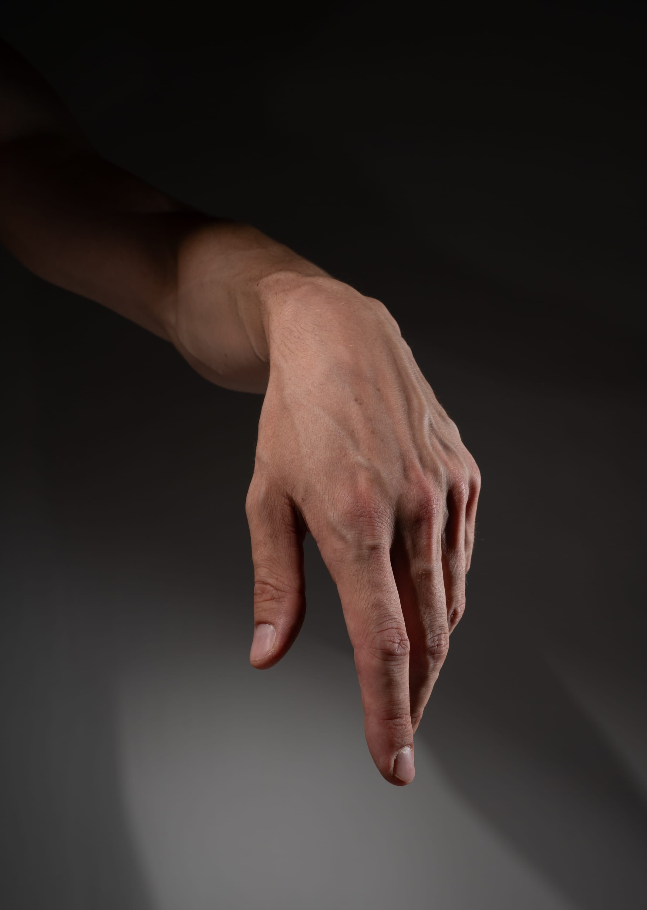 a closeup view of a male hand and forearm, illuminated by studio lighting to highlight the skin texture and prominent veins.