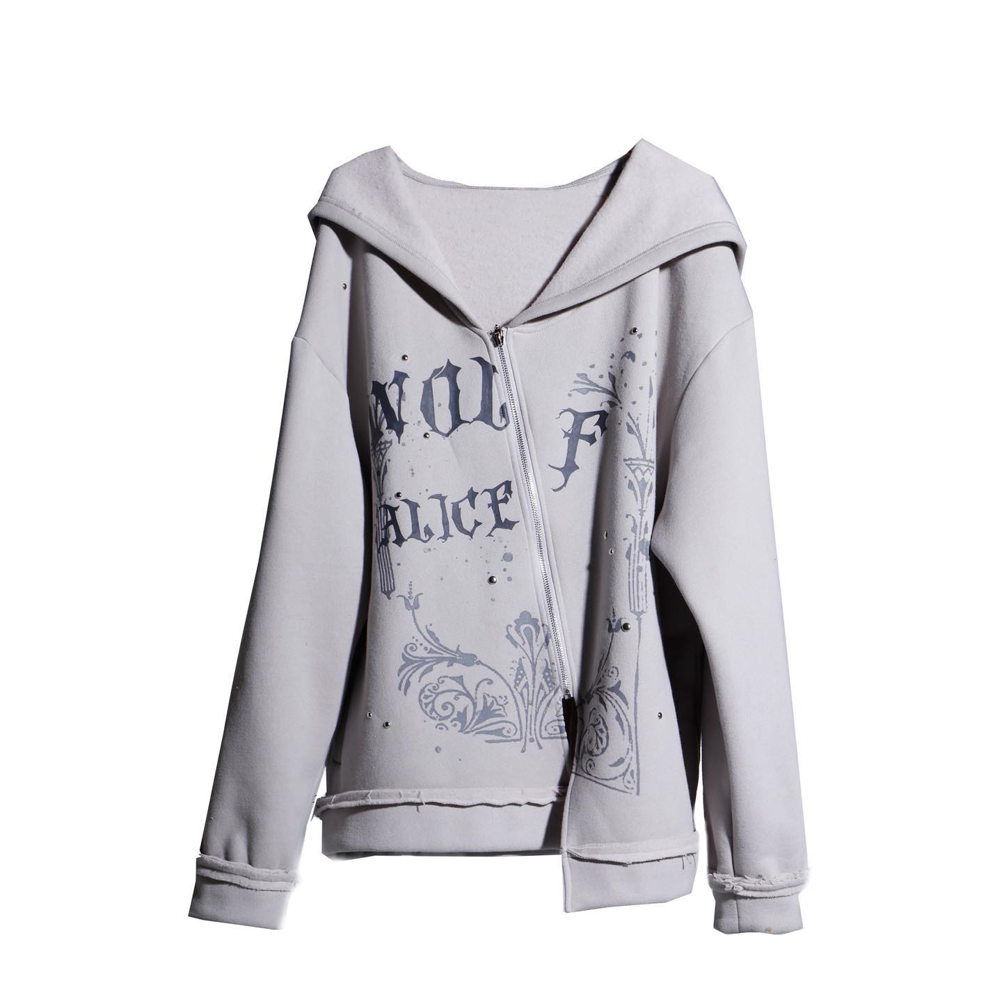 the image shows a women's light grey zipup hoodie. the hoodie features a distressed, slightly oversized fit and has a graphic print on the front. the print incorporates text that appears to say "now f alice" in a gothicstyle font, accompanied by decorative floral and architectural elements.  the hoodie is presented on a white background, showcasing its details clearly.