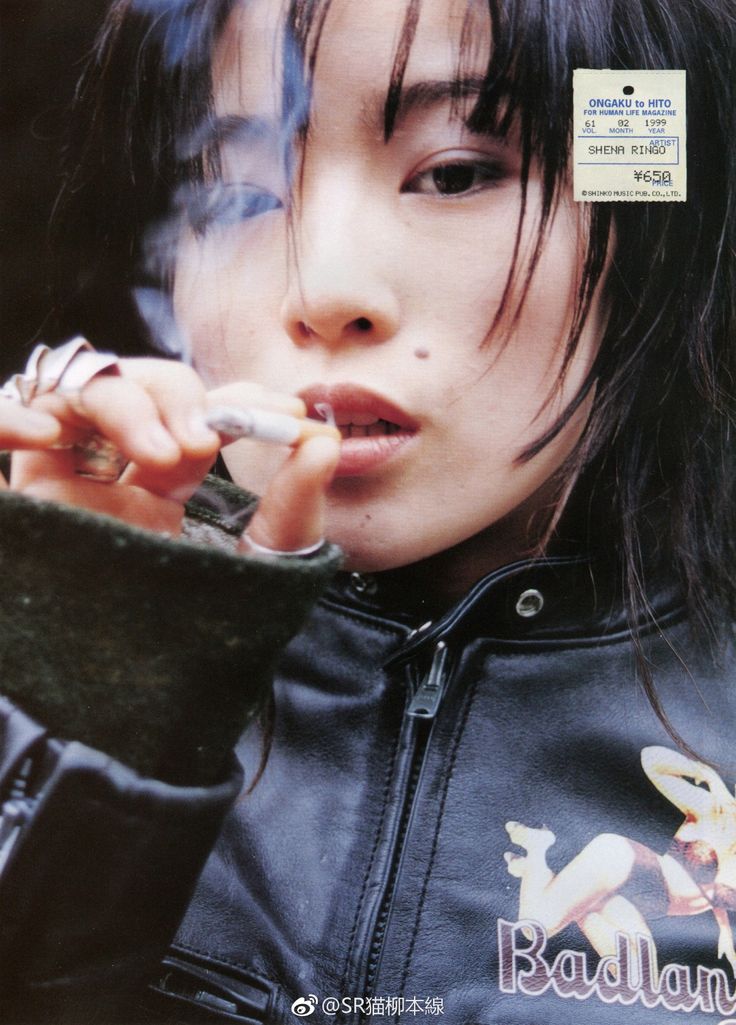 closeup monochrome portrait of the japanese singer shiena ringo, from a 1999 issue of ongaku to hito magazine. she is smoking a cigarette and wearing a black leather jacket with a graphic on the back.  the image has a grunge aesthetic, reflecting her alternative music style.  a price tag is visible on her jacket.