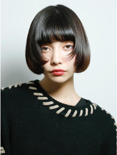 a young asian woman with short black bob haircut with blunt bangs wearing a black sweater with beige trim. she is looking at the camera.  the background is white.
