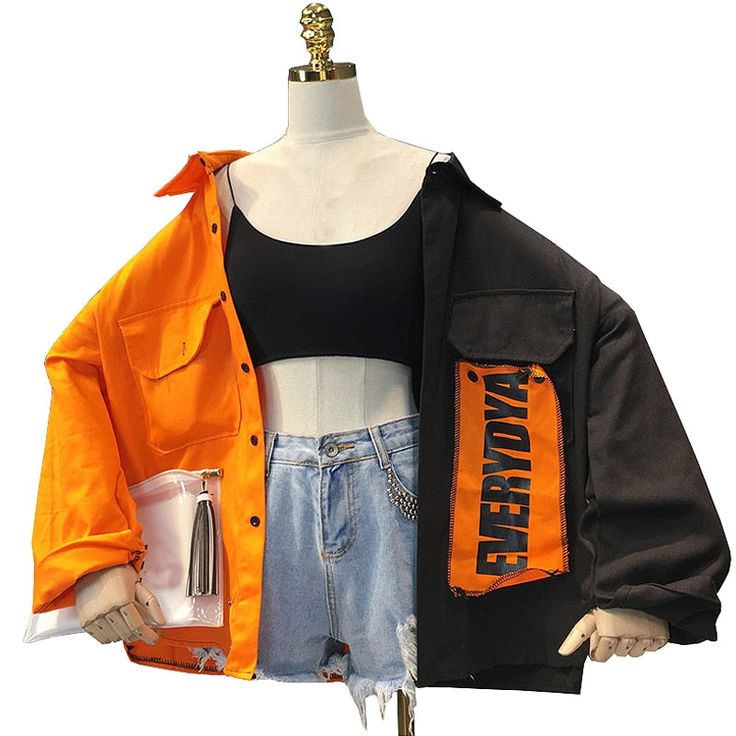 a woman is wearing a black and orange jacket with a white background. the jacket is oversized and has a large orange patch on the right side that says "everyday". the woman is also wearing a black crop top and denim shorts.