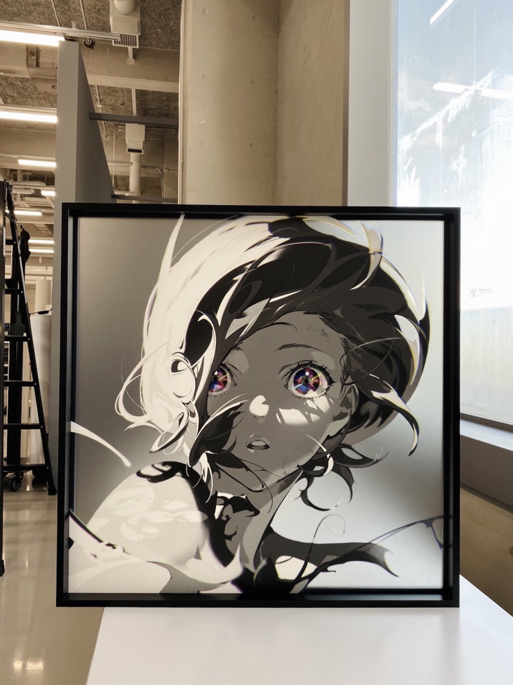 a black and white animestyle drawing of a girl is displayed in a black frame and showcased on a white pedestal in an art gallery. the girl in the drawing has flowing hair and wide eyes, and the artwork is partially colored with vibrant colors in her eyes. the surrounding environment is bright and minimalist, typical of an art gallery setting.