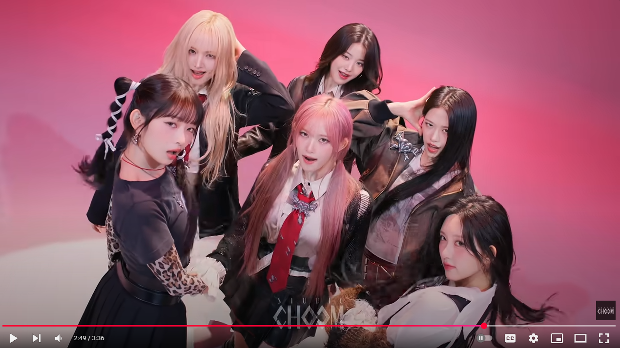 a group of six young women are posing for a photo in front of a pink background. they are dressed in a variety of stylish outfits that blend school uniform elements with modern fashion. the woman on the left wears a black skirt and tshirt with leopard print sleeves, her hair in tied pigtails with white ribbons. the woman beside her wears a blonde wig and a blazer. the central figure has pink hair in pigtails and a red tie. behind her, another woman smiles with long brown hair. to the right, another woman touches her hair and is wearing a jacket, while a girl with long dark hair is near her. in the bottom right corner is the studio choom logo.