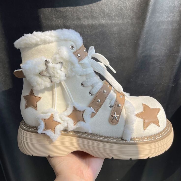 a pair of white platform boots with fur trim around the top and a star pattern across the top of the shoe. the laces are white and the buckles are silver. the sole is a beige color.