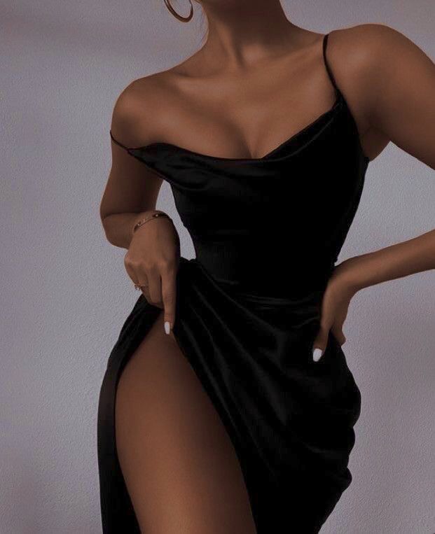 a woman is posing in a black slip dress with a thighhigh slit. she has jewelry on her wrist and a ring on her finger. she has white nail polish.