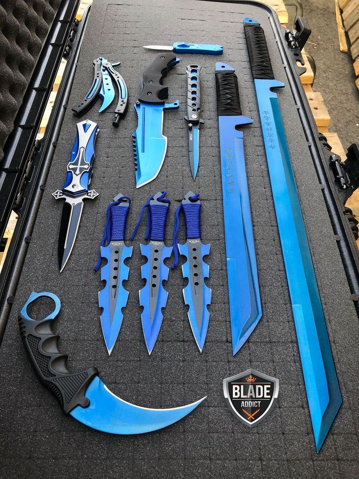 the image shows a collection of bluethemed knives, blades, and swords arranged neatly in a black case. there's a karambit with a curved blade and a black handle, several throwing knives with blue cords, a butterfly knife, a dagger with a silver and black handle, a knife with a partially serrated blue blade and a black handle, a small stilettostyle knife, a tanto, and a couple of swords with blue blades. the "blade addict" logo is in the bottom right corner.