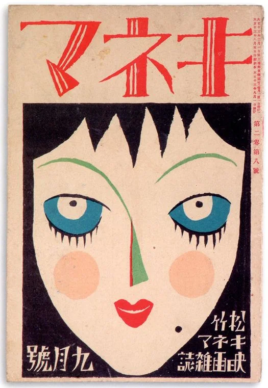 this is a vintage japanese magazine cover featuring a stylized illustration of a woman's face. the woman has fair skin, blue eyes with thick black lashes, green eyebrows and nose, red lips, and rosy cheeks. her hair is black and cut in a sharp, geometric style. the background behind her hair is also black, creating a strong contrast with her face. red japanese text is printed above the woman's face, and black japanese text appears in the lower corners of the image. the cover has a worn and aged appearance, suggesting it is from the early 20th century. the overall style is reminiscent of art deco and japanese modernism.