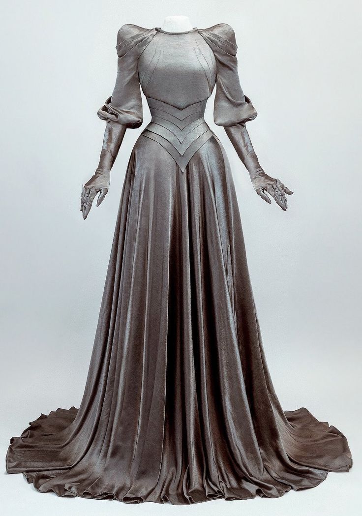 a fulllength studio shot shows a silvercolored velvet gown with long sleeves and matching gloves, displayed on a mannequin. the gown features a high neckline, a fitted bodice with geometric detailing at the waist, and a floorlength skirt with heavy draping and a slight train. the long sleeves are puffed at the shoulder and taper to the wrists, covered by matching gloves. the mannequin is placed against a neutral backdrop.