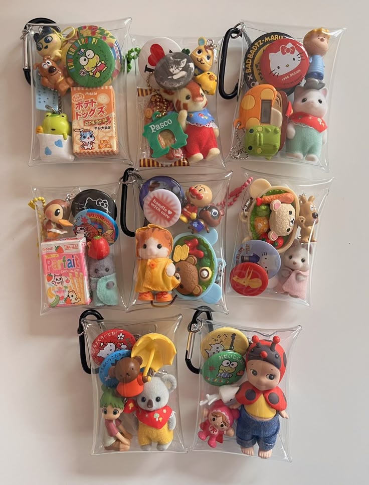 the image shows a collection of nine transparent bags filled with various toys, keychains, and badges. the bags appear to be organized on a white surface. the contents of the bags include characters from sylvanian families, sanrio's kerropi and hello kitty, bad badtzmaru, and anpanman. there are also miscellaneous dolls such as a ladybug doll, a koala doll, a bear doll, a cat doll, a dog doll, a giraffe doll, a mouse doll, and a frog doll. the bags also contain various snacks such as potato dog snacks, parfait snacks, and pasco pastries.