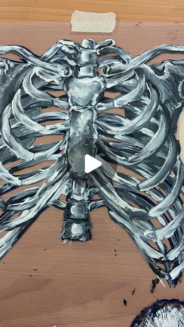 a timelapse video showing the progression of a rib cage painting. the rib cage appears to be lifesized, and is painted in shades of white, grey, and black on a tan surface.