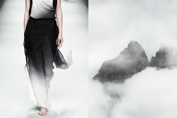 a woman in a black and white ombre dress walks down a runway in front of a backdrop of misty mountains. the dress is simple yet elegant, and the woman's hair is pulled back to accentuate her features. the mountains in the background are shrouded in fog, creating a sense of mystery and intrigue. the overall image is minimalist and sophisticated, with a strong emphasis on the beauty of both fashion and nature.