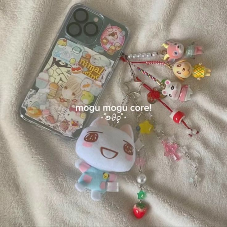 the image shows a phone case with a clear case that has a collage of animal crossing character stickers inside. attached to the case is a series of charms. these include animal crossing characters, a stuffed animal crossing character wearing a blue outfit, stars, beaded accessories and a strawberry. the background is a textured white blanket.