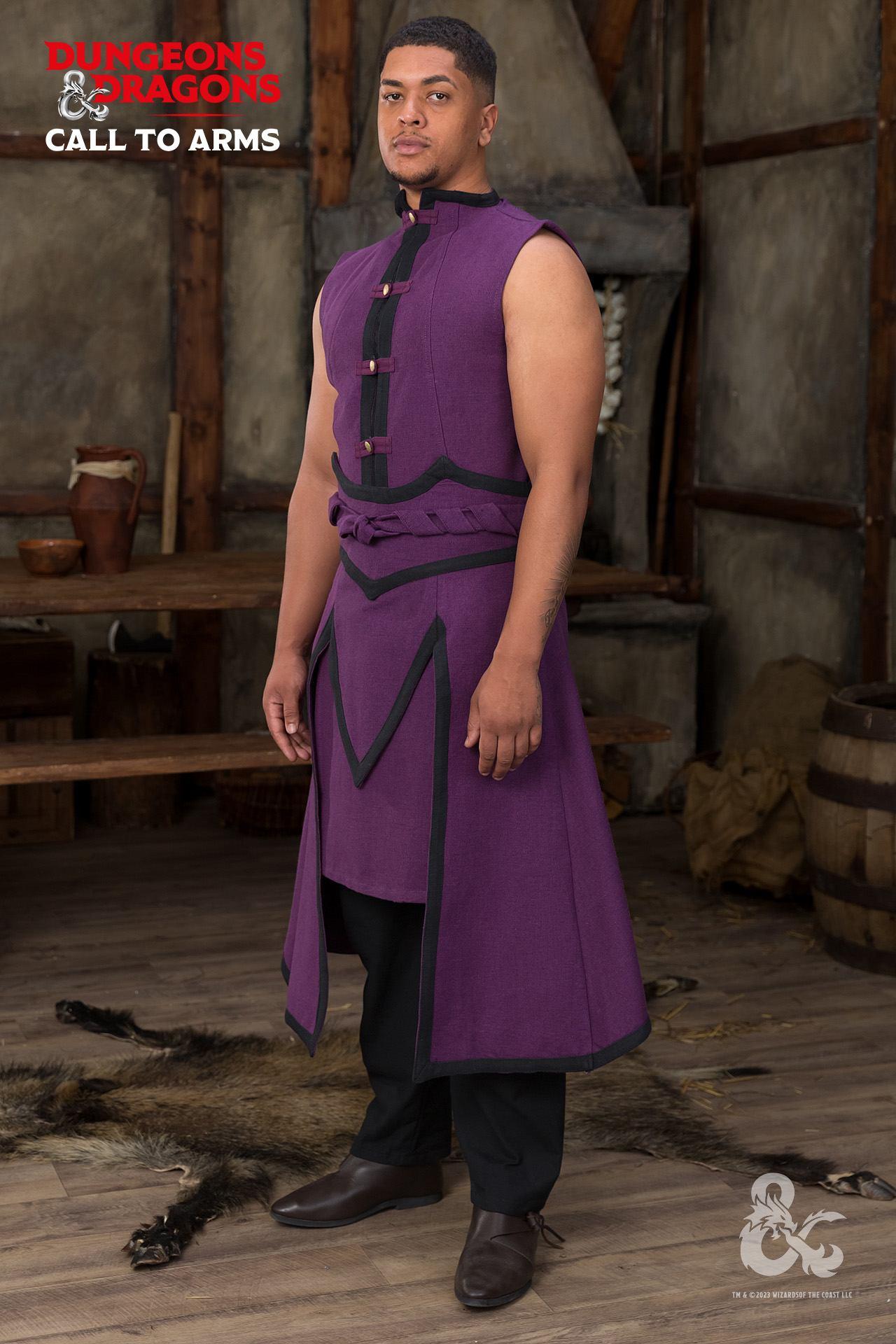 a full shot of a man indoors. the man is wearing a purple tunic with black trim, black pants, and brown shoes. the tunic has a high collar and is sleeveless. the man is standing in front of a wooden table and a fireplace. there is a fur rug on the floor. the image is promoting a "dungeons and dragons" costume.