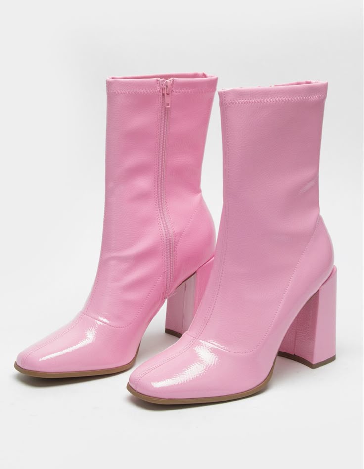 the image shows a pair of pink, shiny patent leather ankle boots with square toes and block heels. the boot on the left has a zipper closure.