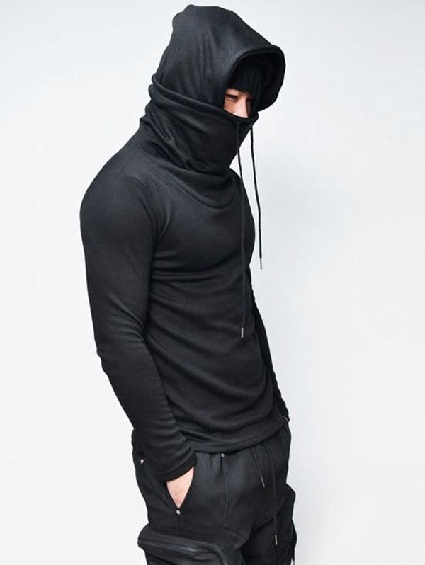 a man is wearing a black long sleeve turtleneck hoodie with a high neck collar. he has a black beanie pulled down over his eyes. he is wearing black cargo pants. he is looking down at the camera and has a cool and trendy look. he is posing in a casual and relaxed manner. the photo was taken in a white background. the man is most likely a fashion model.