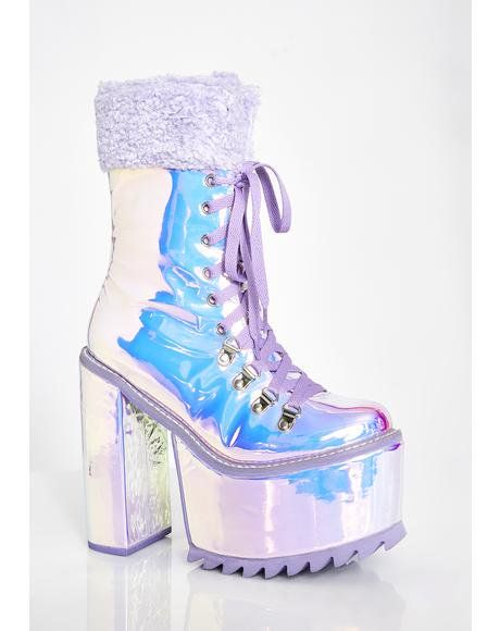 a pair of pastel purple iridescent platform boots with a fluffy purple cuff at the top. the boots are laceup and have a chunky platform heel.  they are shown from a slightly angled perspective against a white background. the boots have a holographic or rainbow effect to their finish.