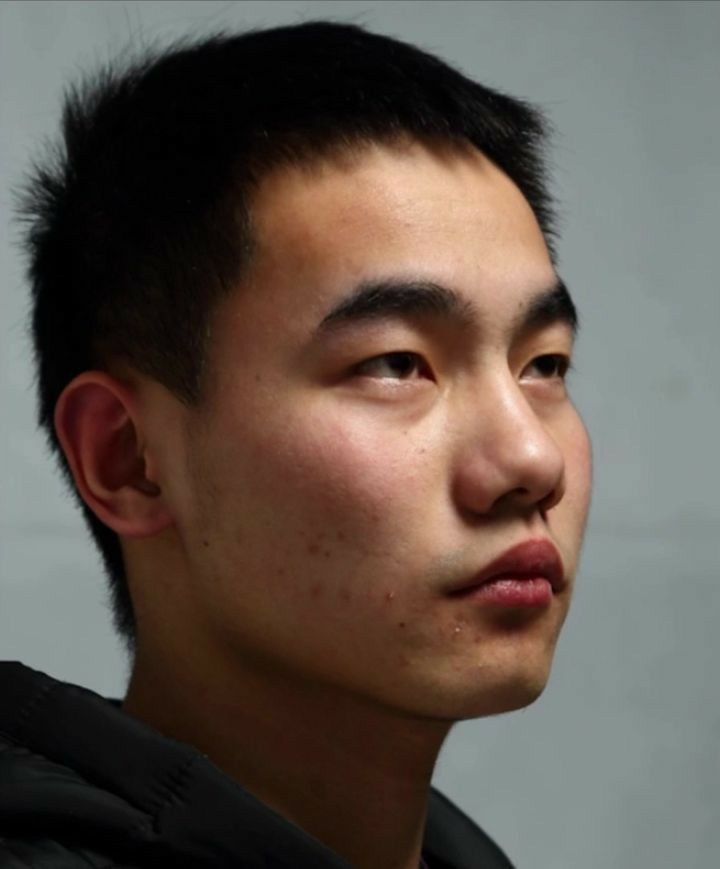 closeup side profile portrait of a young asian man with short dark hair.  his expression is neutral to slightly serious.  the background is a simple, light gray.  his skin is lighttoned and shows some minor acne blemishes. he is wearing a darkcolored hooded jacket. the image is welllit and appears to be a studio shot.