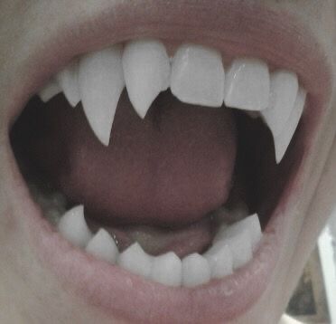a closeup image of a mouth with fangs. the fangs are long and sharp, and the mouth is slightly open. the image is dark and foreboding, and it evokes a sense of fear and danger.