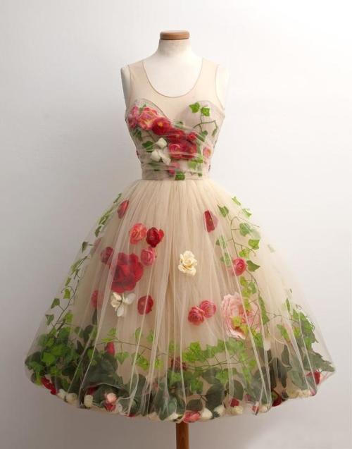 a creamcolored tulle dress with a floral design. the dress is sleeveless and has a scoop neckline. the bodice is fitted and the skirt is full and flares out from the waist. the dress is decorated with red, pink, and white flowers and green leaves. the flowers are arranged in a scattered pattern over the skirt and bodice. the dress is shown on a mannequin. the background is white.