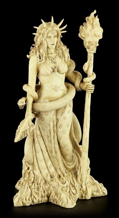 a creamcolored statue of a mythological goddess stands against a black background.  she wears a crown with pointed spikes and holds a burning torch in her right hand. a serpent is wrapped around her body, its head resting near her left hand. the base of the statue appears to be engulfed in flames. the figure is highly detailed, with intricate designs on her clothing and the serpent's scales. the lighting is bright and highlights the statue's features.