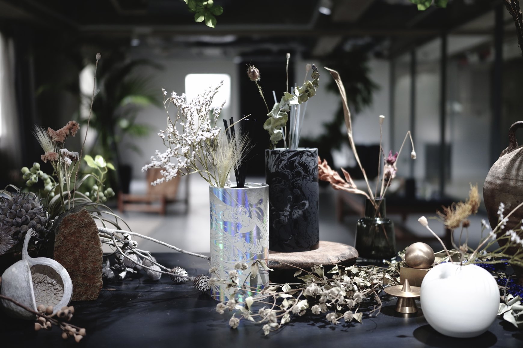 a still life image featuring a collection of vases and dried flower arrangements on a dark table. the scene is set in an indoor environment, likely a home or studio, with a soft and diffused lighting creating a calm and contemplative atmosphere. the image highlights the beauty of natural elements and the artistry of floral design.