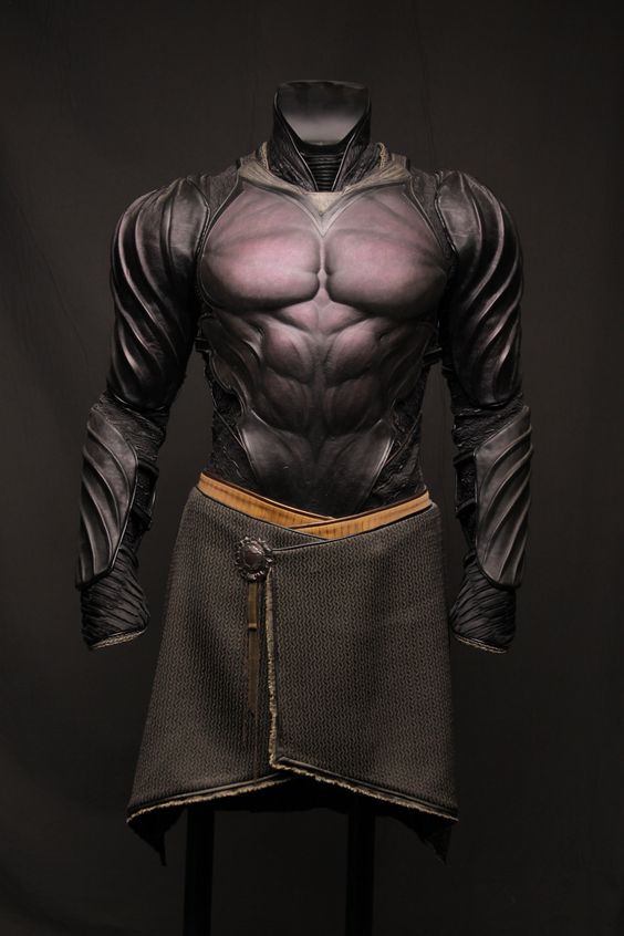 a sculpted torso of a muscular male figure is adorned with intricate black armor. the armor features a breastplate with exaggerated pectoral muscles and segmented arm guards with a ridged, scalelike pattern. a simple brown kilt with a decorative buckle is worn around the waist. the sculpture is displayed against a dark background.