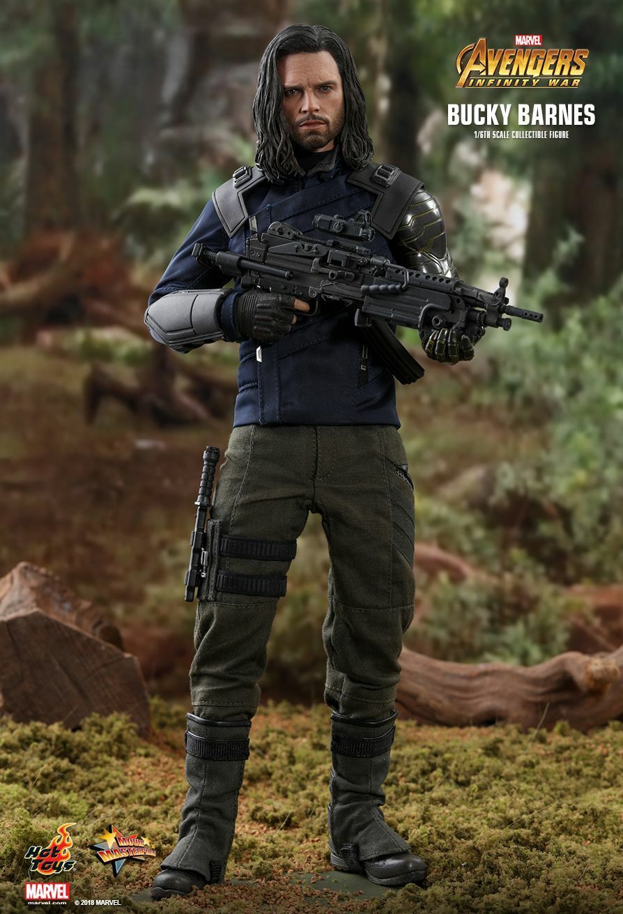 his is a promotional image of a hot toys 1/6 scale collectible figure of bucky barnes from avengers: infinity war. the figure is highly detailed, showcasing bucky's appearance in the film, complete with his dark blue jacket, olive green pants, tactical gear, and his signature metallic arm.  he is holding a machine gun. the backdrop is a blurred forest setting, enhancing the actionfigure's presentation. the image also includes the marvel and hot toys logos.
