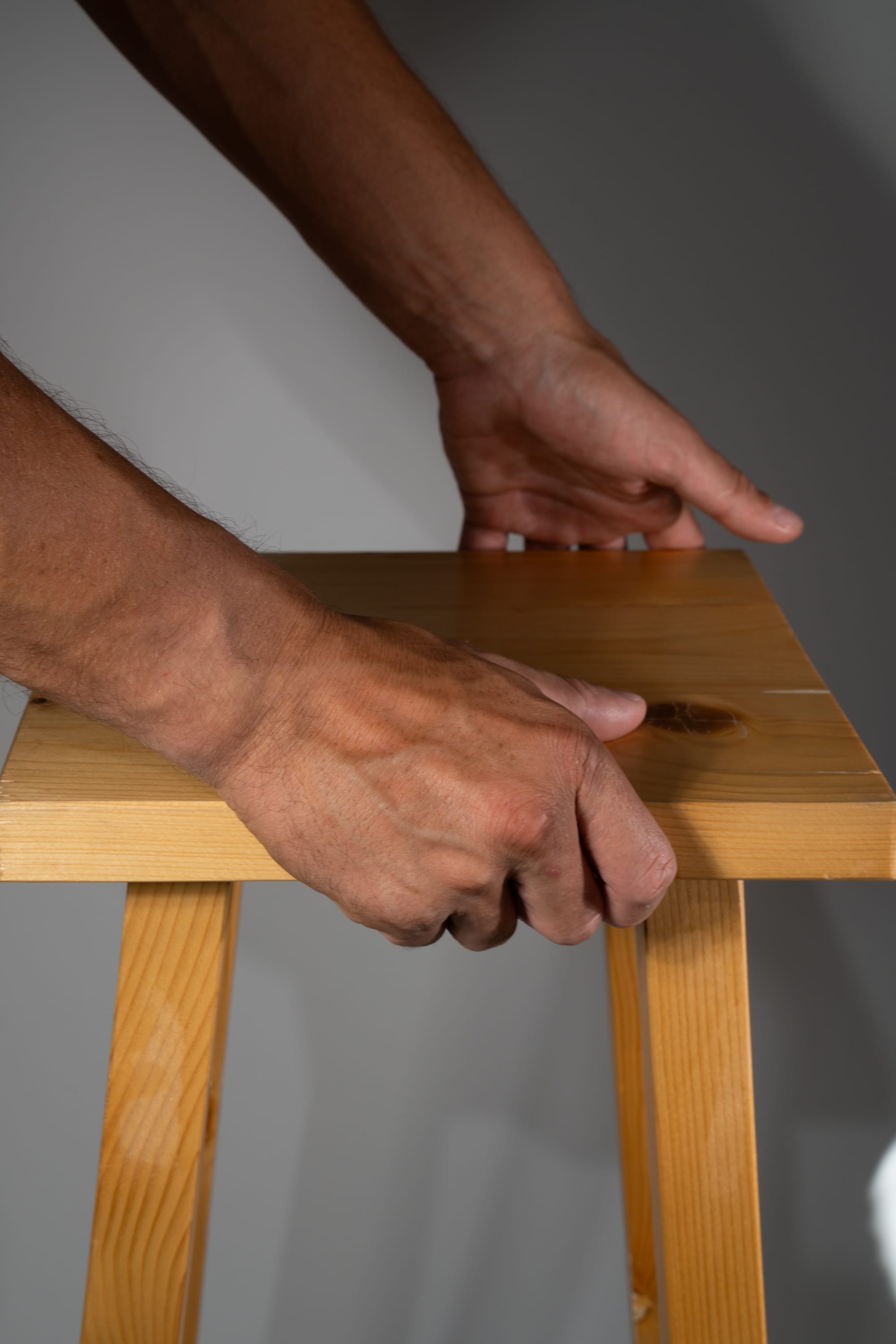 the image shows a closeup view of a man's hands resting on a wooden table. the table is made of light brown wood and has a simple design. the man's arms are muscular and his hands are large and strong. the lighting is soft and natural, creating a warm and inviting atmosphere.