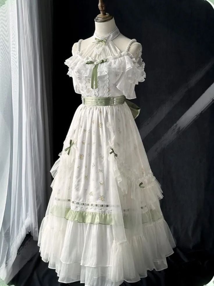 a fulllength studio shot of a beautiful white dress with offtheshoulder sleeves, lace details, ruffles, and a tiered skirt. the dress is adorned with delicate green accents, and it has a feminine and romantic style reminiscent of lolita fashion. the dress is displayed on a mannequin against a dark background.