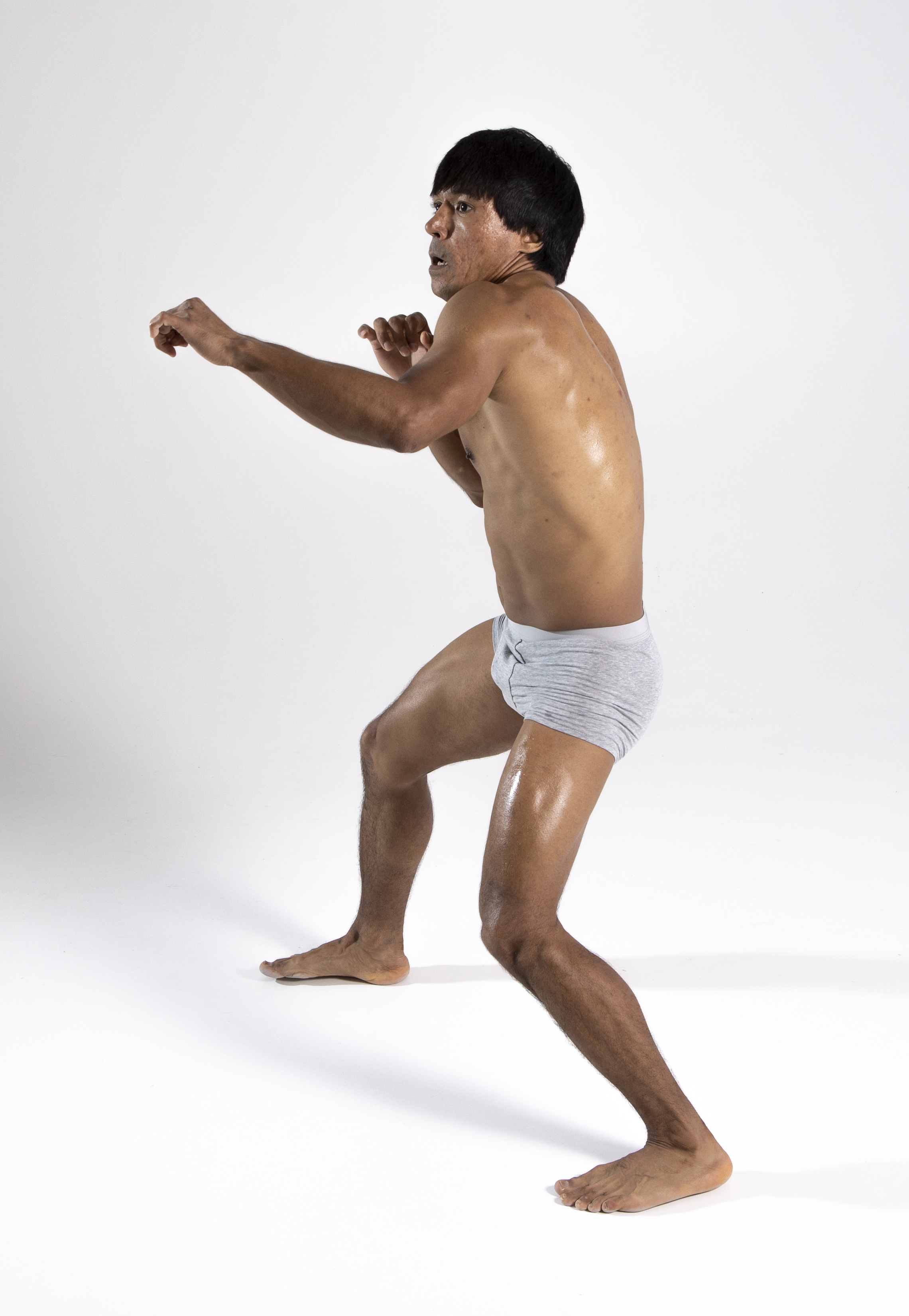 a man in grey underwear stands in a boxing stance with his fists up, in front of a white background. the man's body is sweaty and he is looking to his left.