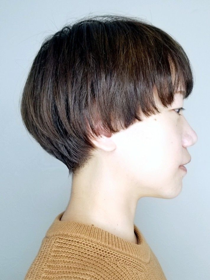 a side profile shot of a young woman with short brown hair styled in a bob cut. she is wearing a brown sweater. her hair is styled in a way that creates a smooth, rounded shape, with her bangs covering her forehead. her profile is sharp and defined, with delicate features. the lighting highlights the texture of her hair and the sheen of her skin, giving the photo a soft and elegant feel.