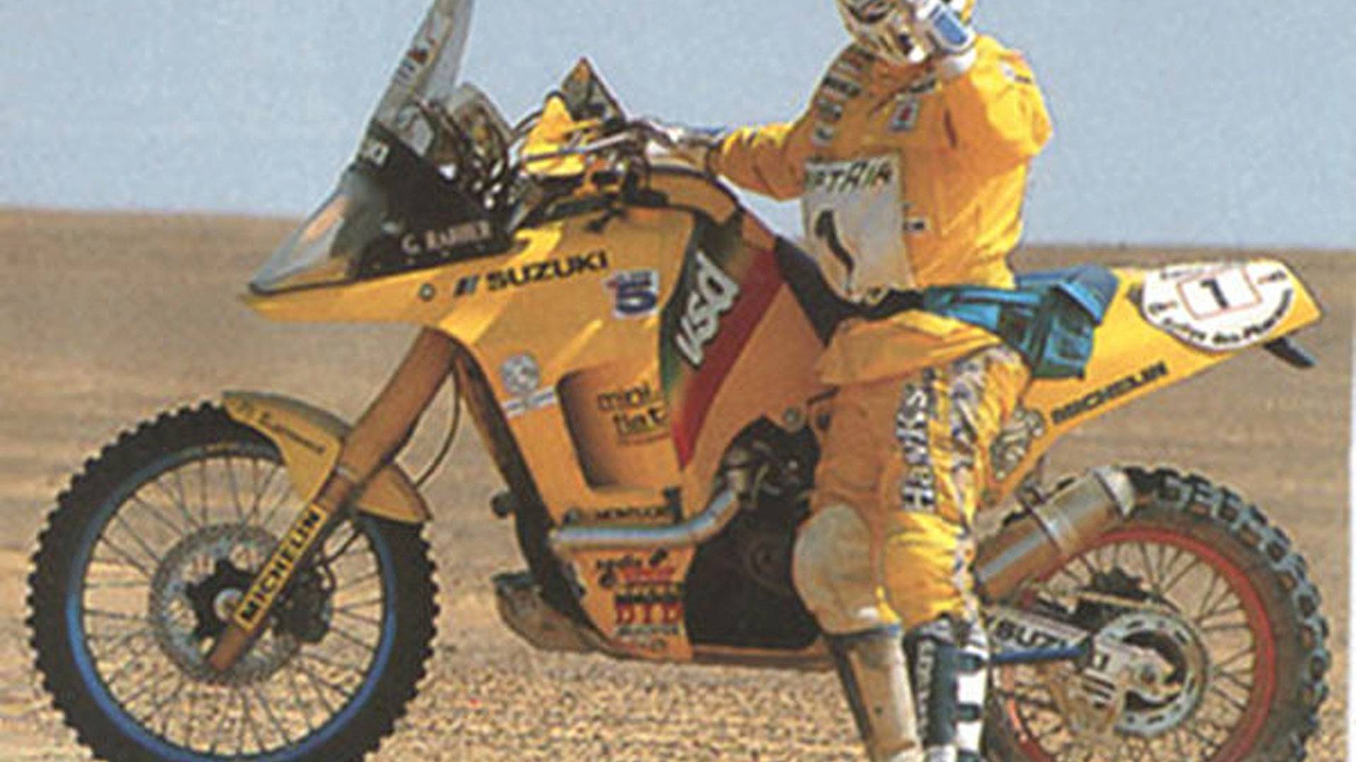 this is a photo of a suzuki motorcycle in the middle of a desert race. the bike is covered in dust and sand, but the rider looks focused and determined. the bike is yellow and blue, with the suzuki logo and other sponsors' logos displayed on the side. the rider is wearing a helmet and goggles, and the background is the desert landscape. the image evokes a sense of adventure, excitement, and speed.