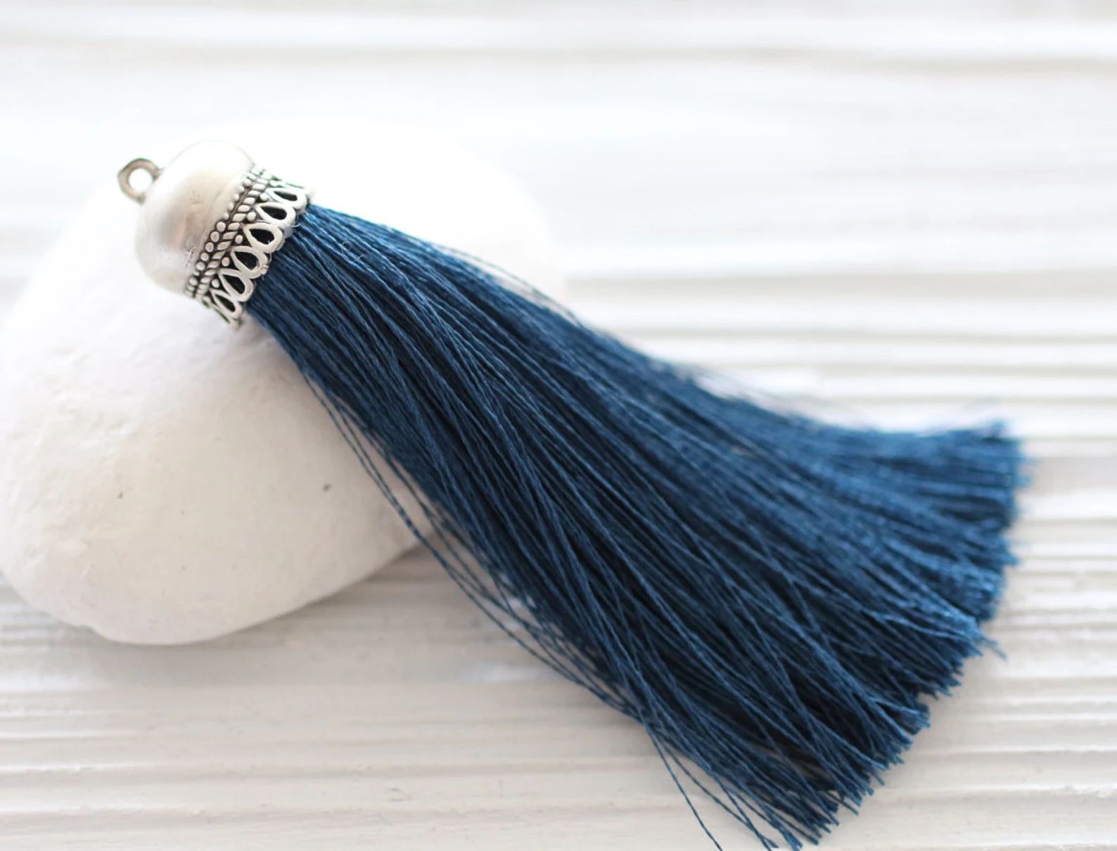 a navy blue silk tassel with a silver cap is laying on a white rock.