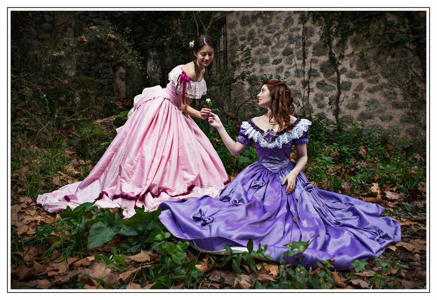 two young women, dressed in elaborate 19thcentury style crinolines, are captured in a moment of gentle interaction amidst a picturesque autumnal setting. one woman wears a soft pink gown, while the other is adorned in a rich purple dress.  they are standing in a wooded area with fallen leaves scattered on the ground. a rustic stone wall forms the backdrop.  one woman is offering a small white flower to the other, suggesting a theme of friendship or shared intimacy.  the atmosphere is serene and romantic. the dresses are highly detailed and historically accurate, exhibiting the full skirts and fitted bodices typical of that era. the overall image is evocative of a romantic period piece or historical photograph.