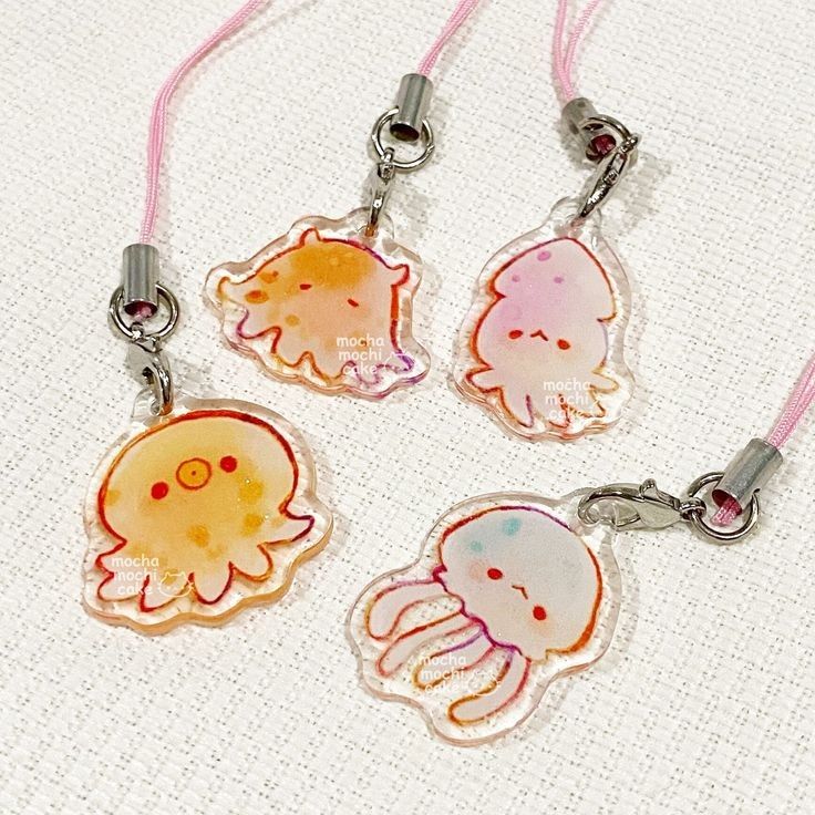 the image features four cartoonstyle acrylic charms hanging from pink cords with metal clasps. the charms depict different sea creatures: an octopus, a squid, and two jellyfish. the artwork is kawaiiinspired, with each creature having a cute, simple face. a logo "mocha mochi cake" is printed on each charm.