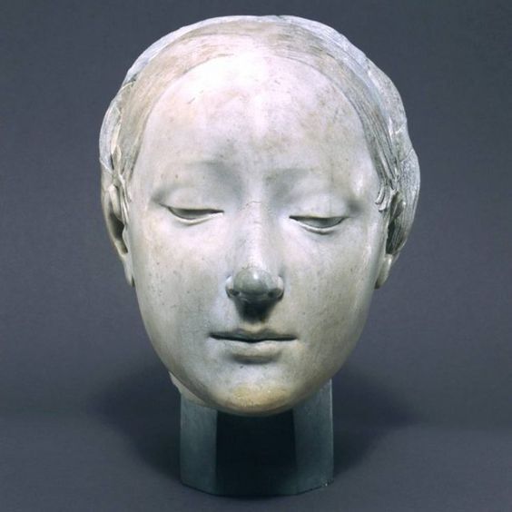 a bust sculpture of a female head with closed eyes. the sculpture is made of gray stone and has a serene, peaceful expression. it is set on a pedestal.