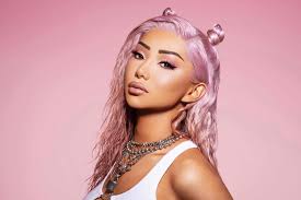 the image is a closeup portrait of a young woman with long, wavy, pastel pink hair styled in space buns. she's wearing a white tank top and several necklaces. her makeup is welldefined, showcasing highlighted features.  the background is a solid, light pink, creating a soft and visually appealing contrast to her hair and clothing. the overall mood of the image is glamorous and stylish, suggesting a possible professional photoshoot for fashion or beauty.  the model appears confident and comfortable, directly engaging the camera.