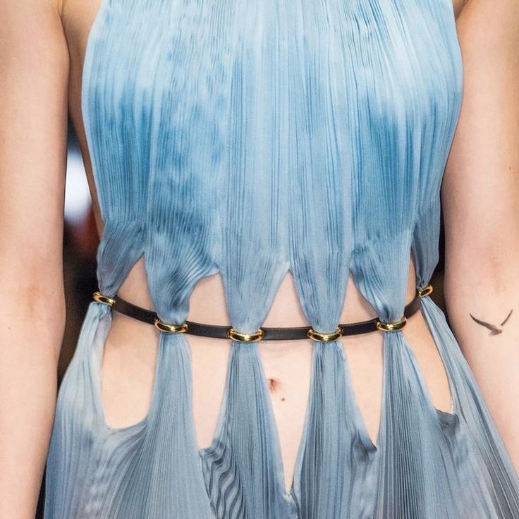 a model walks the runway in a stunning blue pleated dress with cutouts at the waist, adorned with a black belt accented with gold hardware. the dress is elegant and chic, showcasing the latest in high fashion.