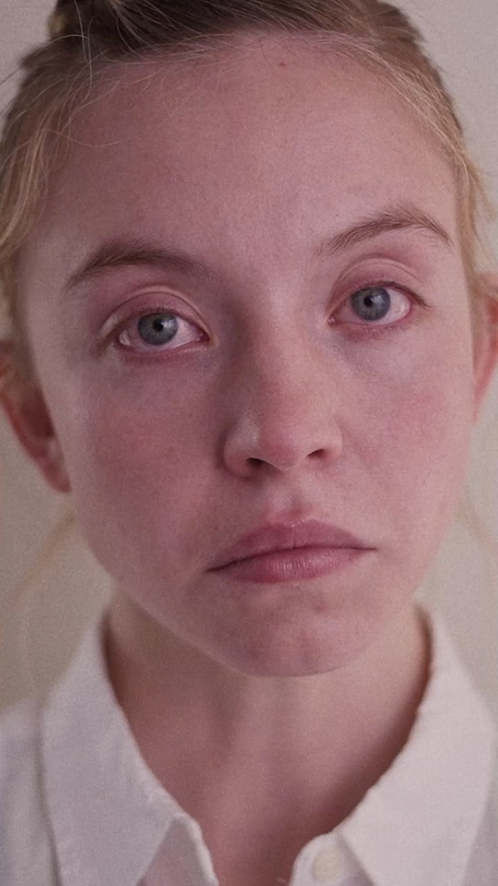 closeup portrait of a young woman with pale skin and light blonde hair pulled back from her face. she's wearing a white collared shirt and has a neutral, slightly serious expression. the background is plain and unfocused, drawing attention to the subject's face. the lighting is soft and even.