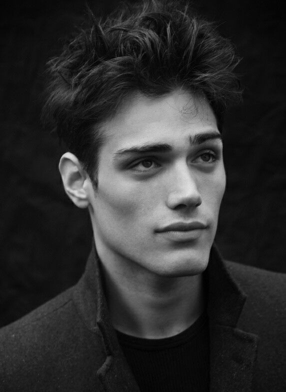 a black and white portrait of a young man with dark, textured hair. he is wearing a jacket and looking slightly off to the side. the image is a closeup headshot with a focus on his facial features.