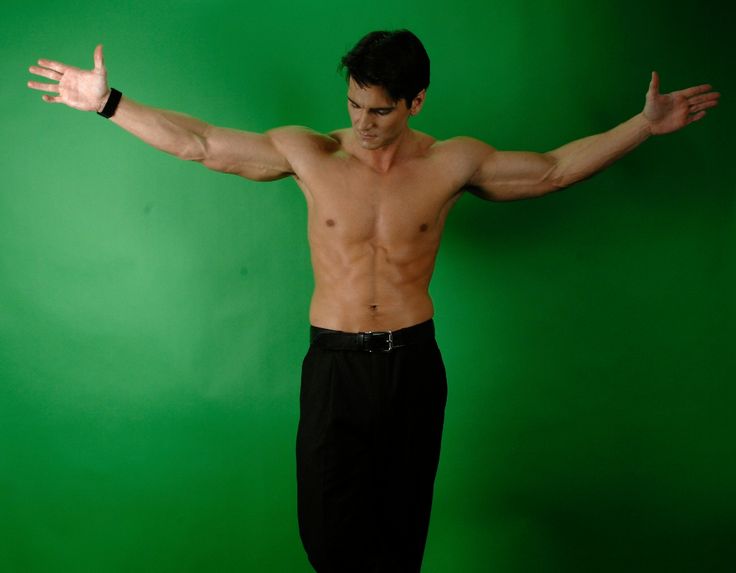 a shirtless, muscular man poses against a green screen, with his arms outstretched. he is clearly athletic and has defined abs.