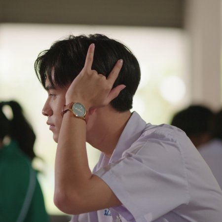a closeup side profile of a young man, likely a student, in a classroom setting. he's wearing a white uniform shirt and a wristwatch. his hand is raised to his head in a gesture of contemplation or listening. the lighting is soft and natural, likely coming from a window. the overall mood is peaceful and thoughtful.