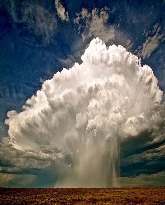 a dramatic view of a huge rain cloud with dark storm clouds in the background, and a rain curtain falling from it.