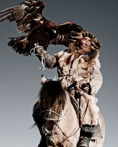 a kazakh eagle hunter is seen riding a horse, with a golden eagle perched on his gloved hand. he is wearing traditional fur clothing and a distinctive hat. the scene evokes the ancient tradition of falconry in central asia, highlighting cultural heritage and a symbiotic relationship between humans and birds of prey.