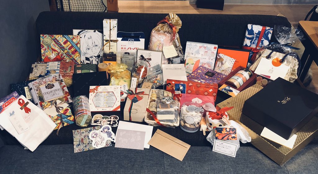 a couch covered with many gifts wrapped in colorful wrapping paper. the gifts are of different shapes and sizes, and some have ribbons and bows on them. there are also some cards and envelopes scattered among the gifts.
