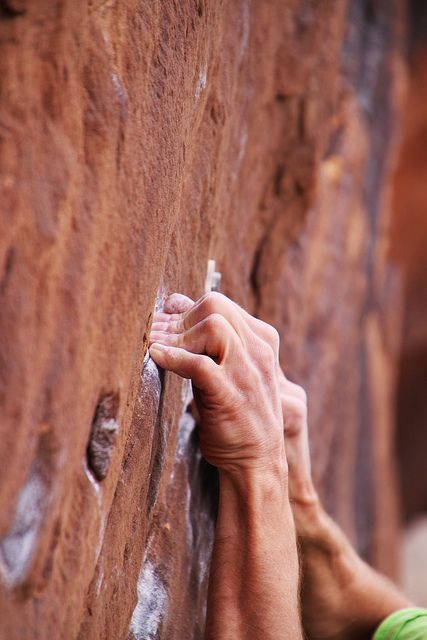 a closeup shot of a rock climber's hand gripping a rock wall. the climber's hand is positioned on a hold, with the fingers extended and reaching for another hold. the focus is on the climber's hand and the texture of the rock wall. the climber's arm is visible, and the image captures the strength and dexterity required for rock climbing.