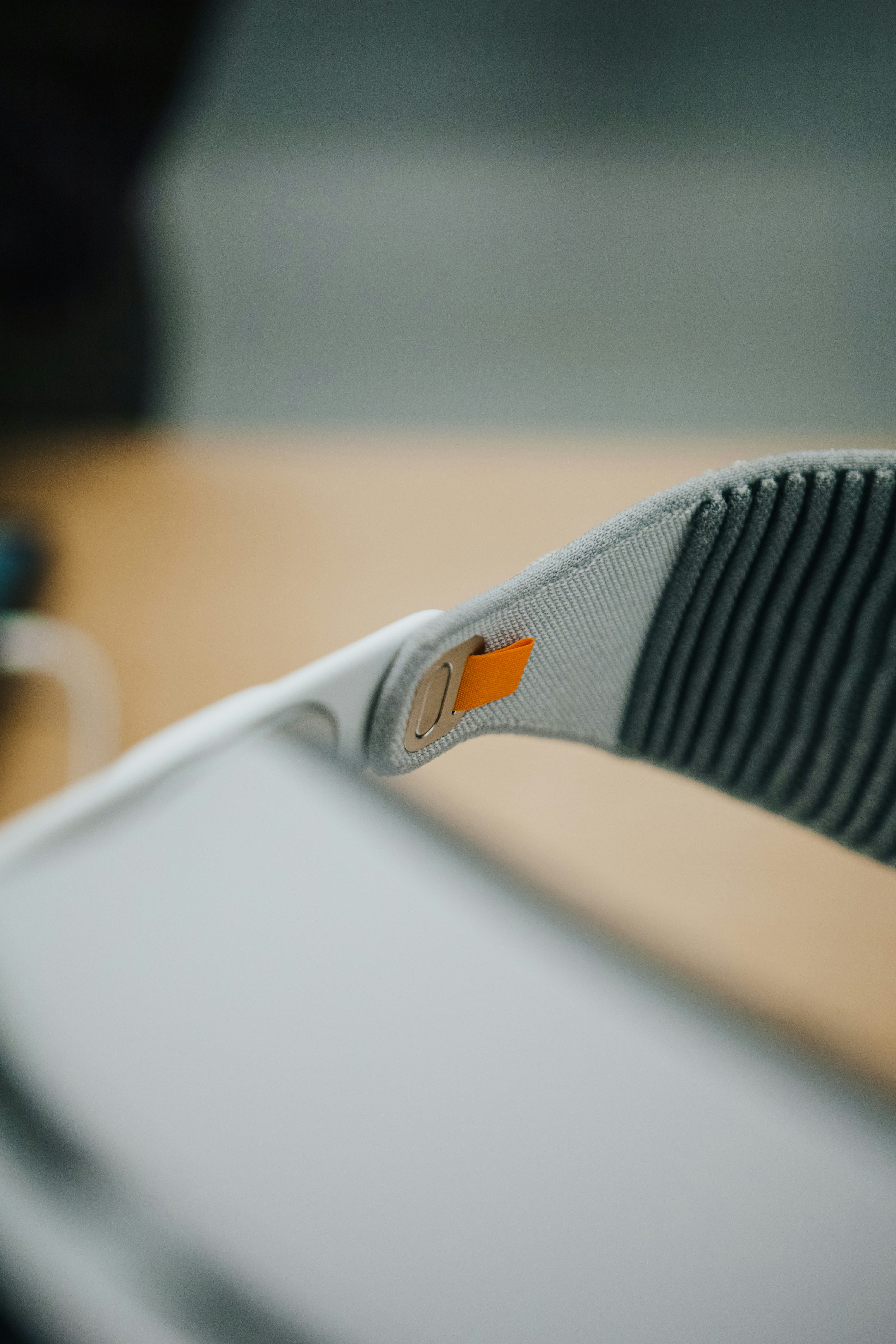 a closeup shot of a meta quest 2 virtual reality headset, focusing on the gray strap with an orange tab. the device appears to be resting on a lightcolored surface with a blurred background.